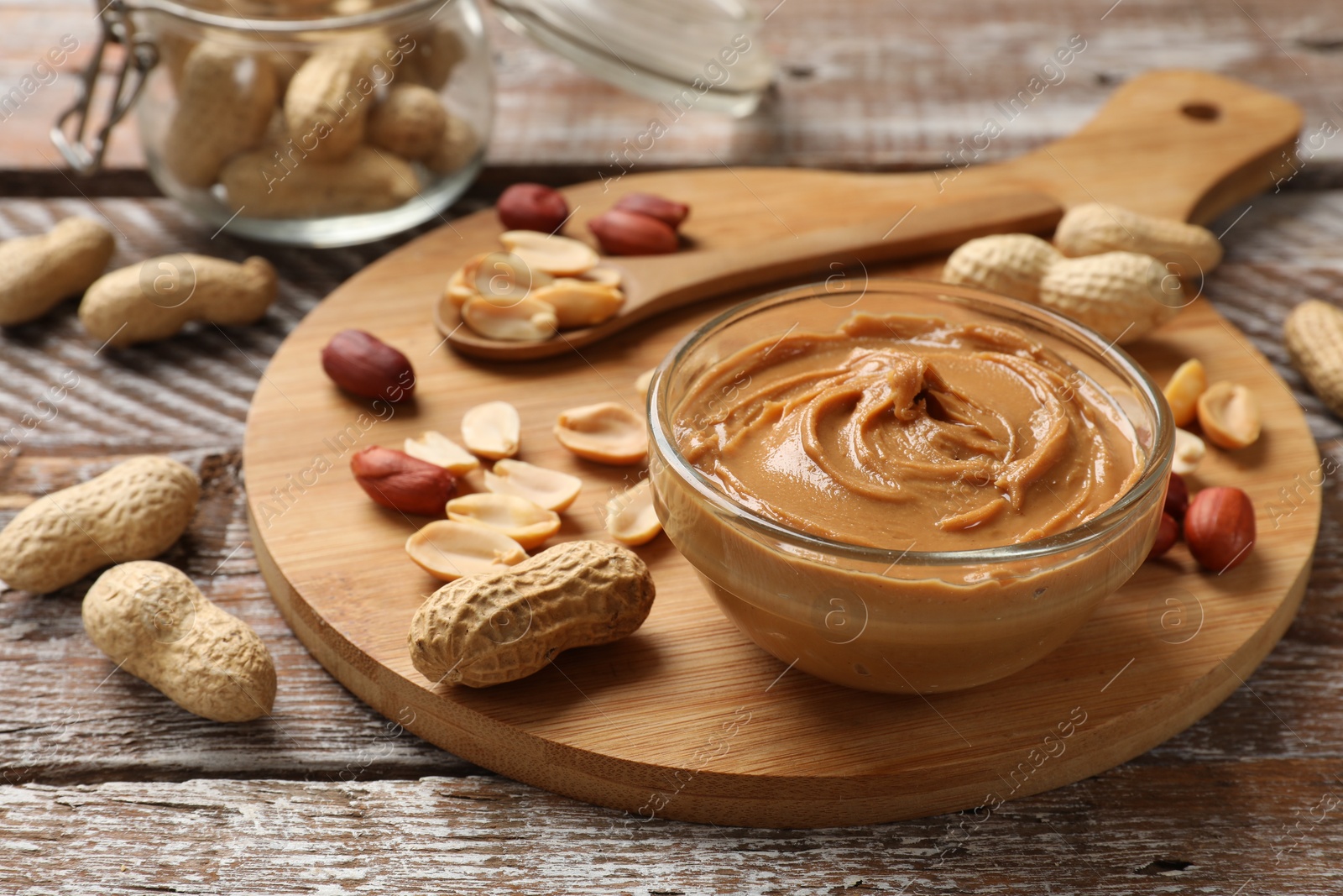 Photo of Tasty peanut butter in bowl and groundnuts on wooden table