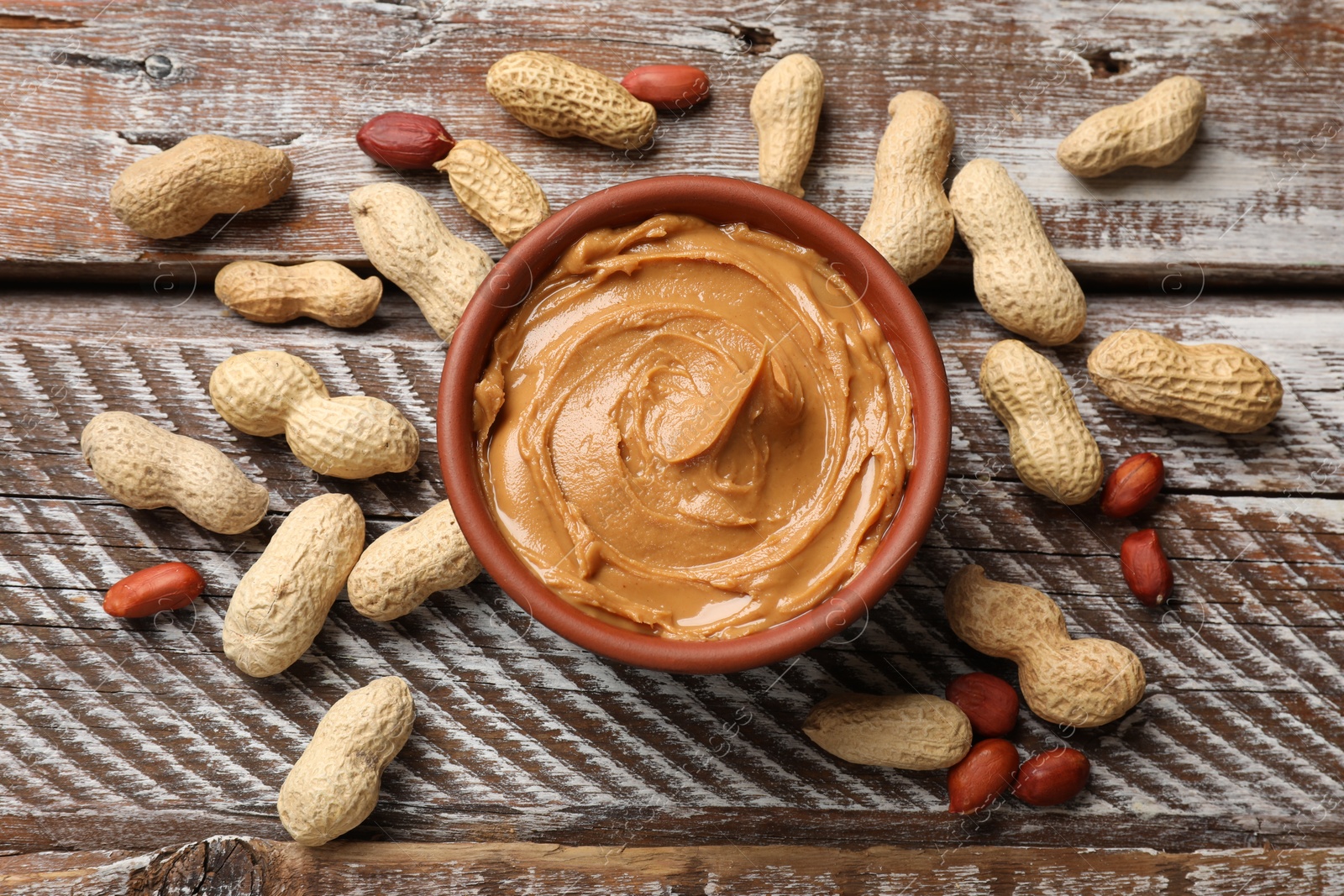 Photo of Tasty peanut butter in bowl and groundnuts on wooden table, flat lay