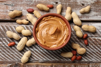 Tasty peanut butter in bowl and groundnuts on wooden table, flat lay