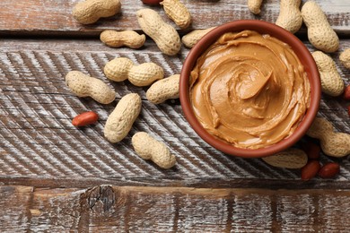 Photo of Tasty peanut butter in bowl and groundnuts on wooden table, flat lay