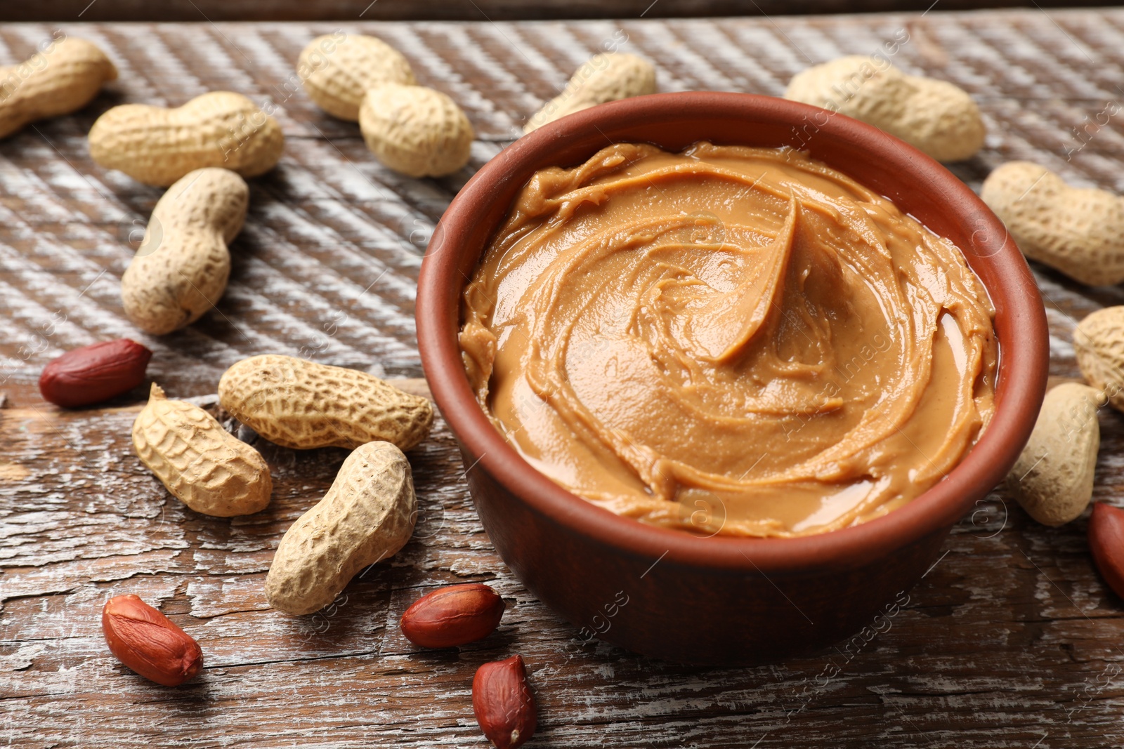 Photo of Tasty peanut butter in bowl and groundnuts on wooden table, closeup