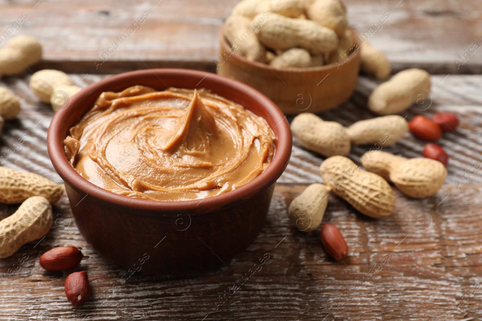 Photo of Tasty peanut butter in bowl and groundnuts on wooden table, closeup