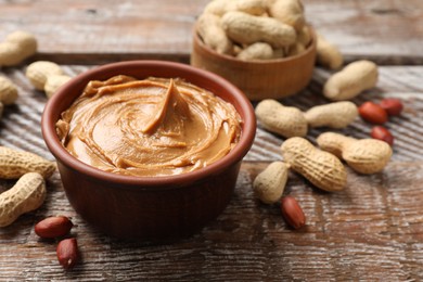 Photo of Tasty peanut butter in bowl and groundnuts on wooden table, closeup