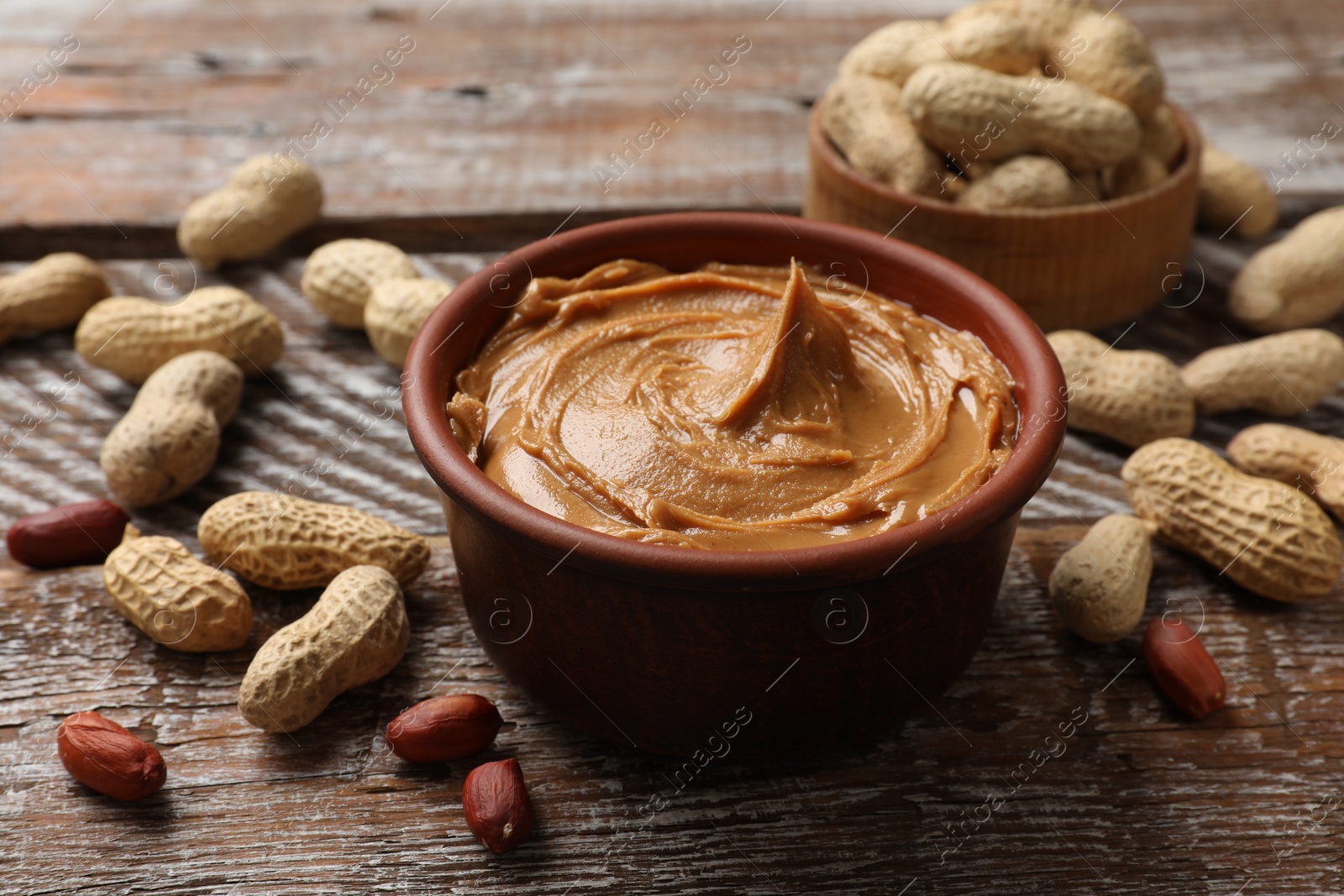 Photo of Tasty peanut butter in bowl and groundnuts on wooden table, closeup