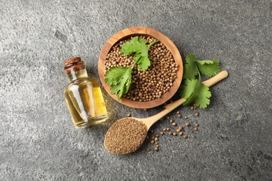 Photo of Coriander essential oil, powder, seeds and green leaves on grey table, top view