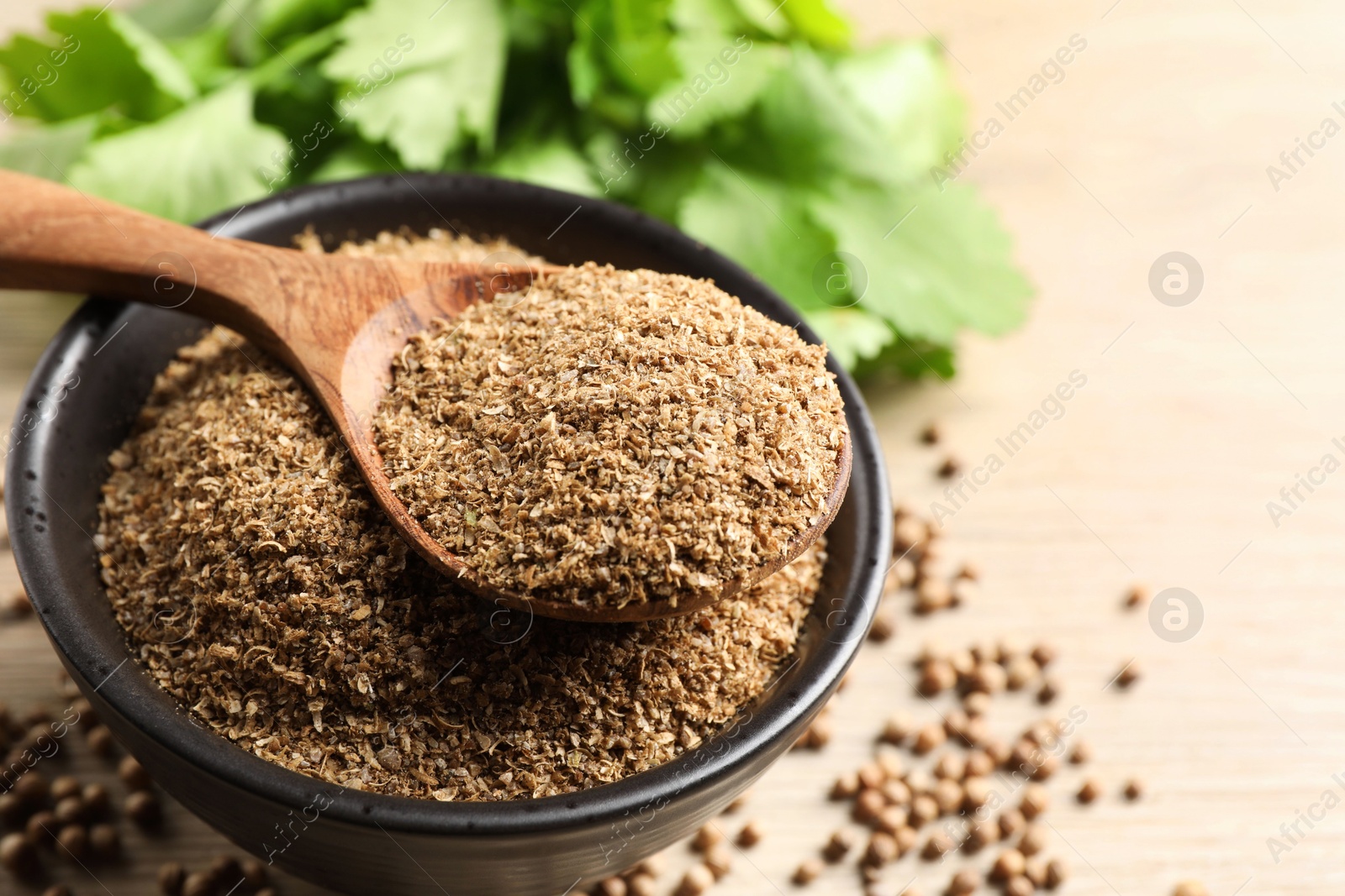 Photo of Coriander powder in bowl, spoon, seeds and green leaves on table, closeup