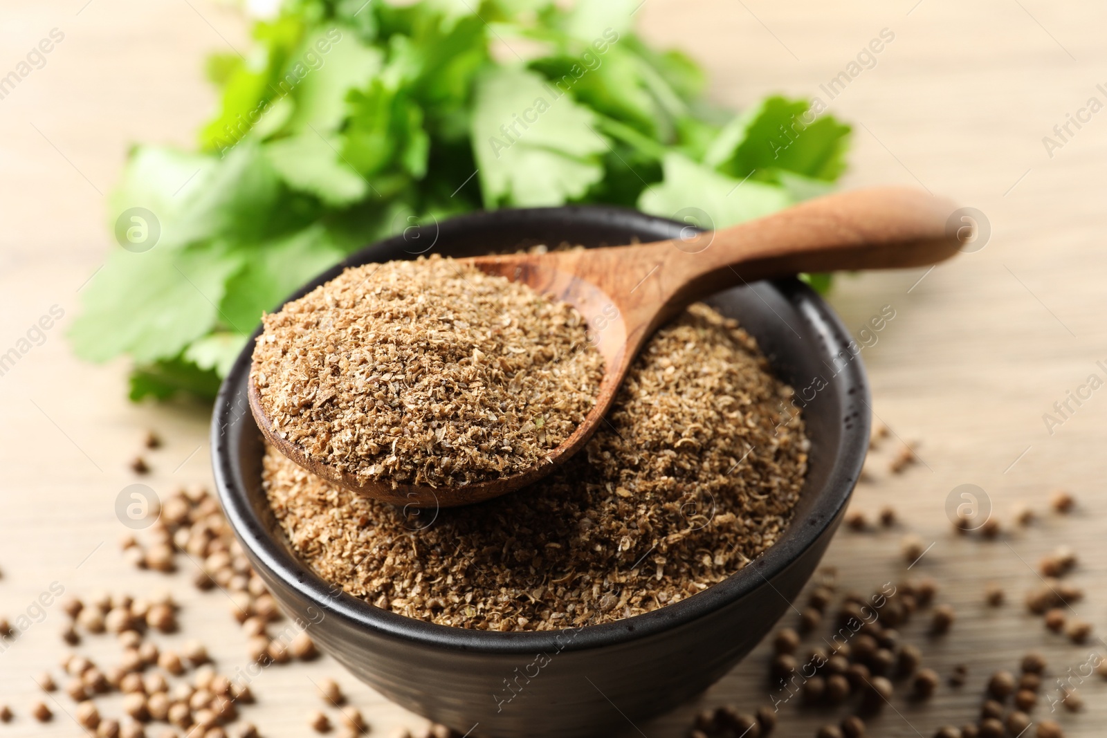 Photo of Coriander powder in bowl, spoon, seeds and green leaves on wooden table, closeup