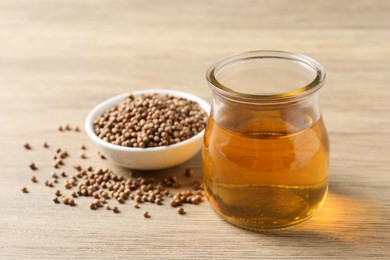 Photo of Dried coriander seeds in bowl and oil on wooden table