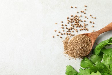 Coriander powder in spoon, seeds and green leaves on light grey table, above view