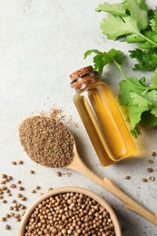 Coriander essential oil, powder, seeds and green leaves on light grey table, flat lay