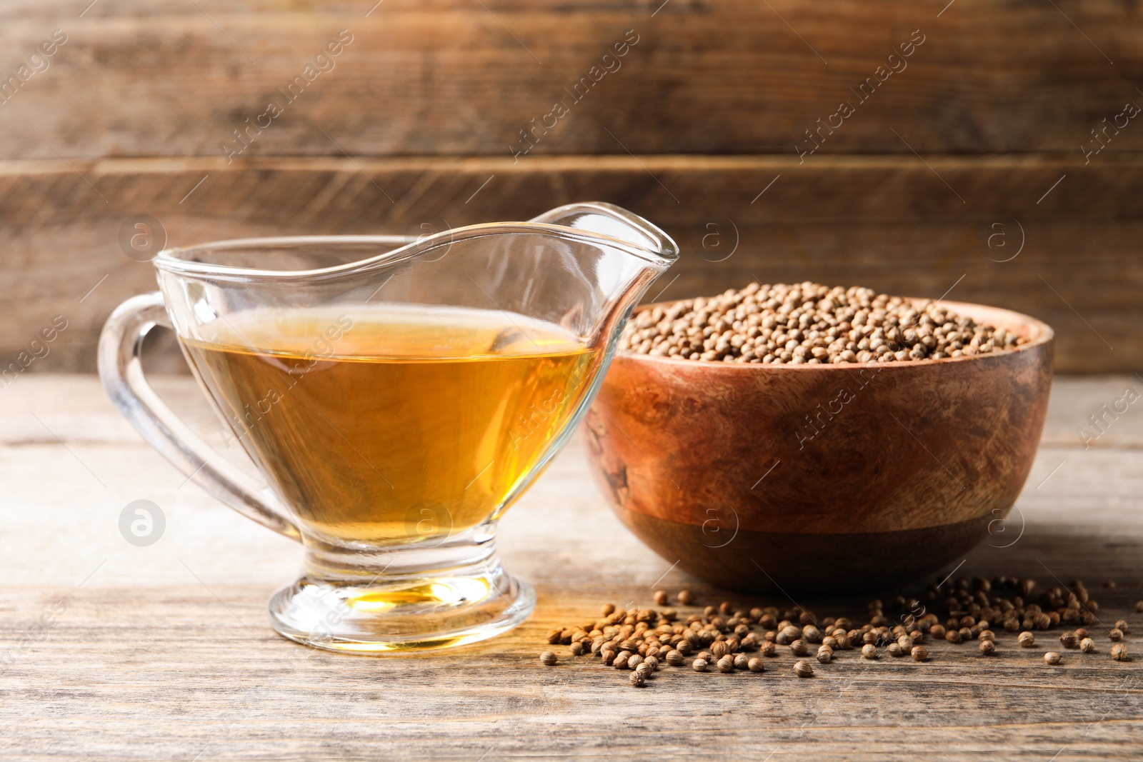 Photo of Dried coriander seeds in bowl and oil on wooden table