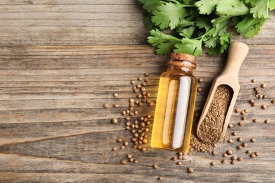 Photo of Coriander essential oil, powder, seeds and green leaves on wooden table, top view. Space for text