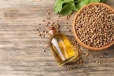 Photo of Coriander essential oil, seeds and green leaves on wooden table, top view. Space for text