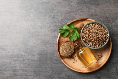 Photo of Coriander essential oil, seeds, powder and green leaves on grey table, top view. Space for text