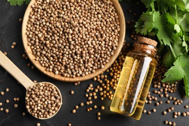 Coriander essential oil, seeds and green leaves on black table, top view