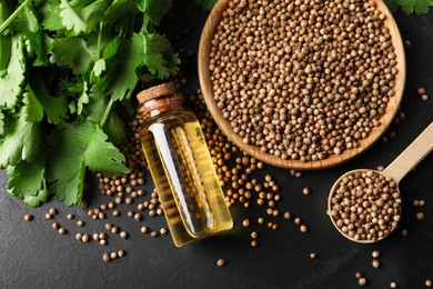 Photo of Coriander essential oil, seeds and green leaves on black table, top view