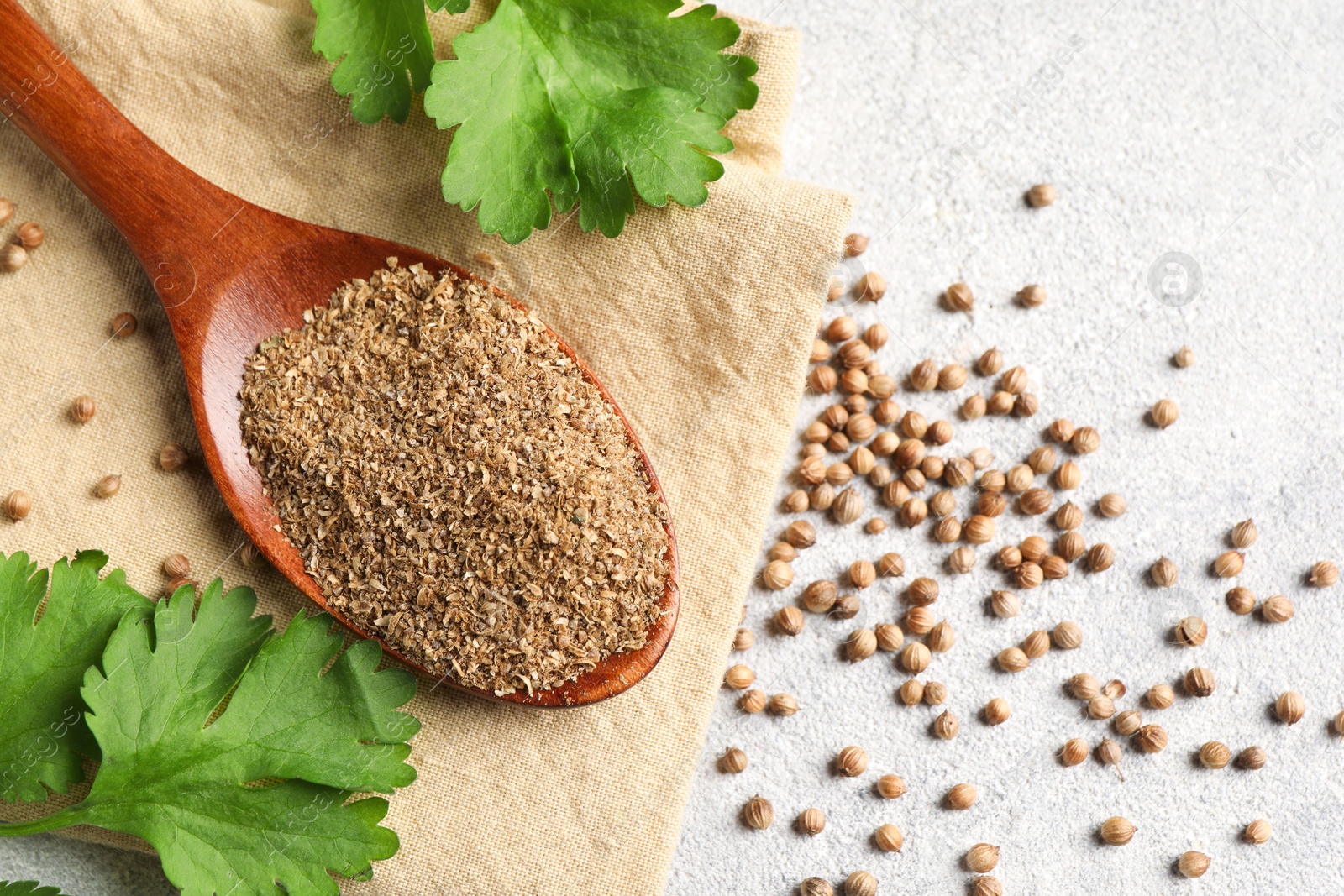 Photo of Coriander powder in spoon, seeds and green leaves on light grey table, top view