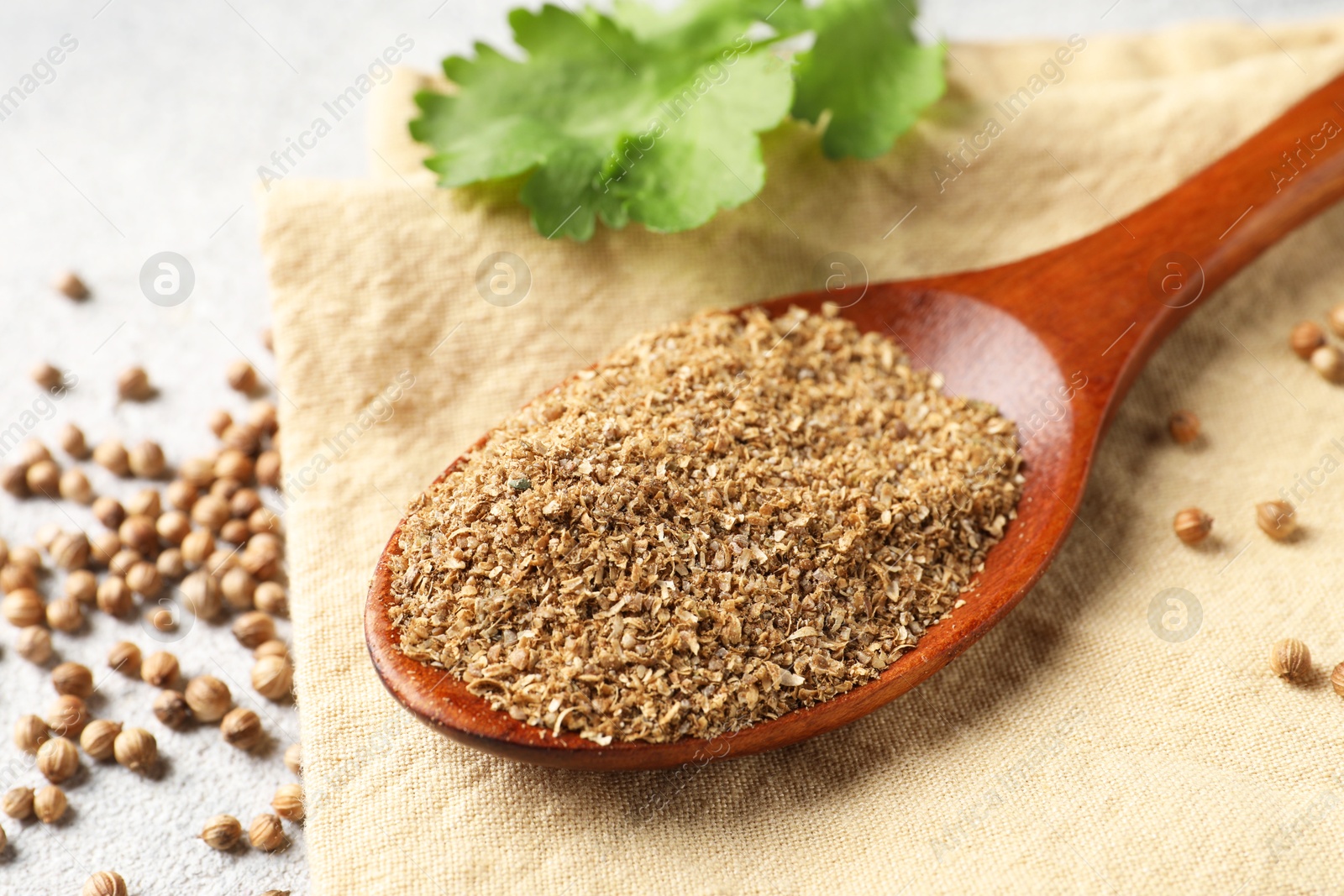 Photo of Coriander powder in spoon, seeds and green leaves on light grey table, closeup