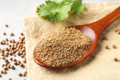 Coriander powder in spoon, seeds and green leaves on light grey table, closeup