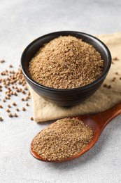 Photo of Coriander powder in spoon, bowl and seeds on light grey table