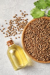 Coriander essential oil, seeds and green leaves on light grey table, top view