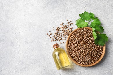 Coriander essential oil, seeds and green leaves on light grey table, top view. Space for text