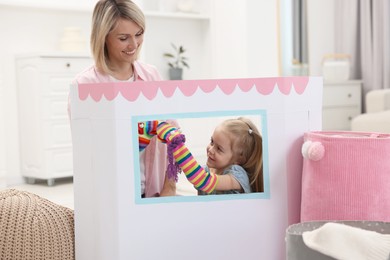 Photo of Puppet theatre. Girl playing toys with her smiling mother at home