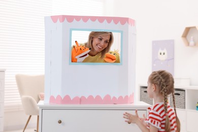 Photo of Puppet theatre. Smiling mother performing show with toys to her daughter at home