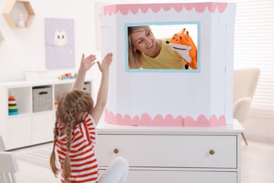 Photo of Puppet theatre. Smiling mother performing show with toy to her daughter at home