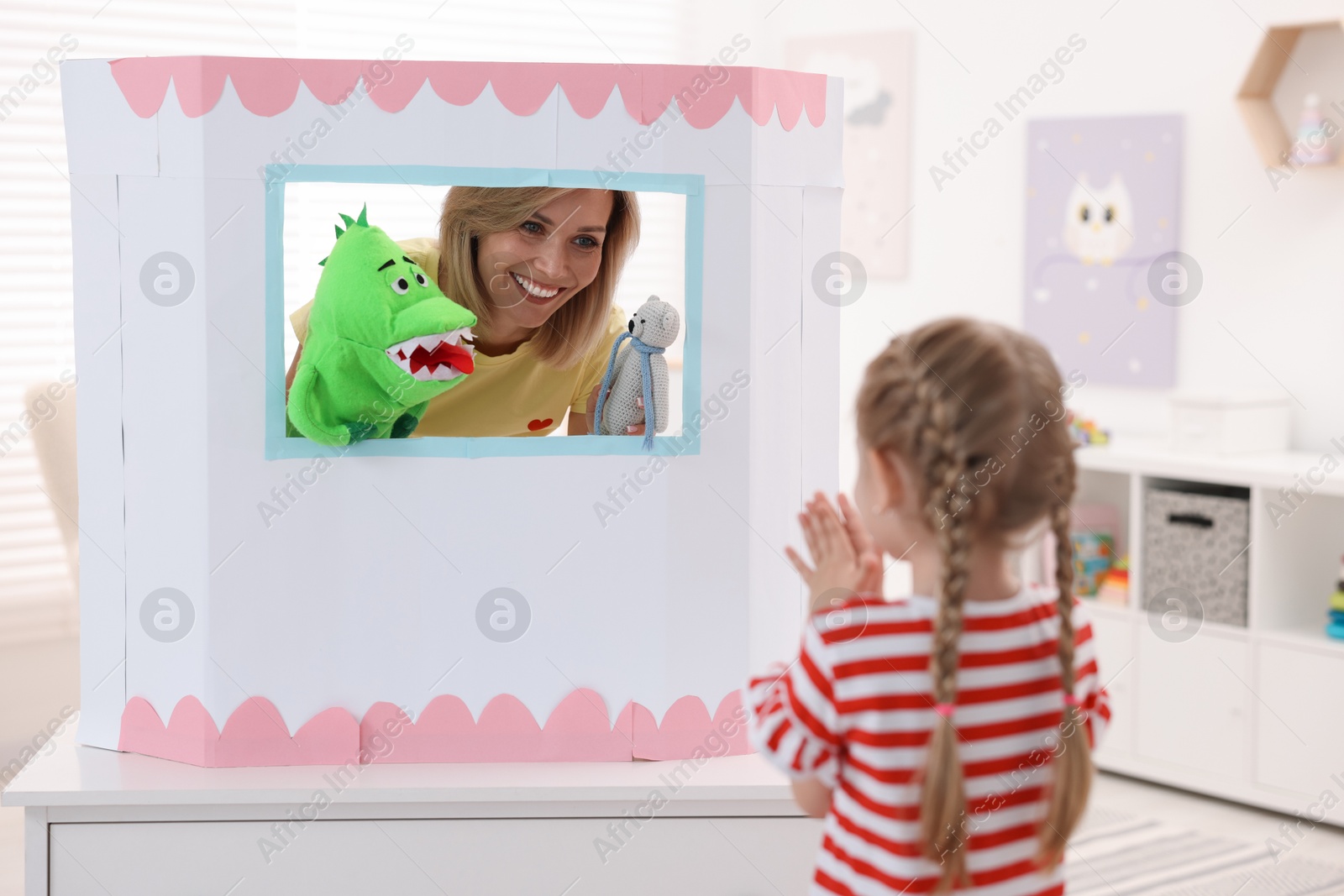 Photo of Puppet theatre. Smiling mother performing show with toys to her daughter at home