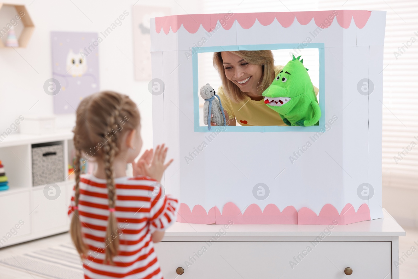 Photo of Puppet theatre. Smiling mother performing show with toys to her daughter at home