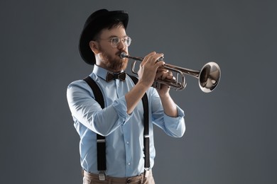 Handsome musician playing trumpet on grey background