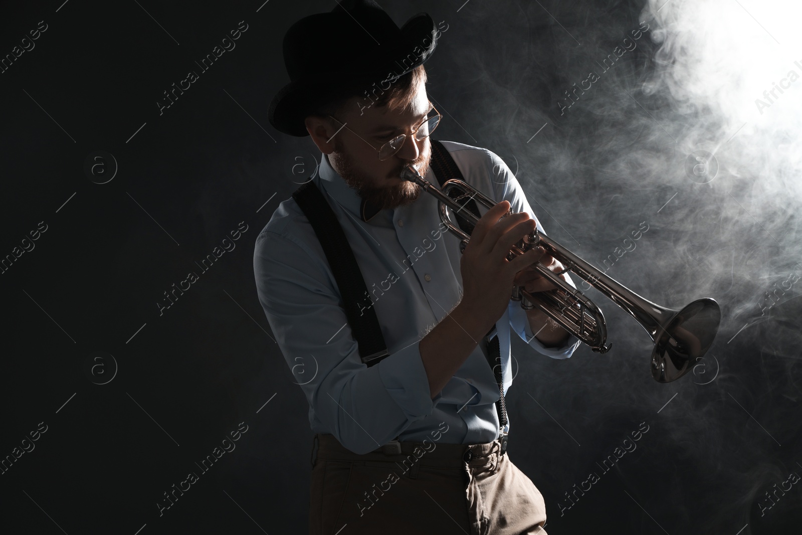 Photo of Professional musician playing trumpet on black background with smoke