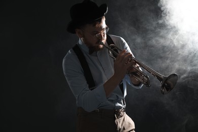 Professional musician playing trumpet on black background with smoke