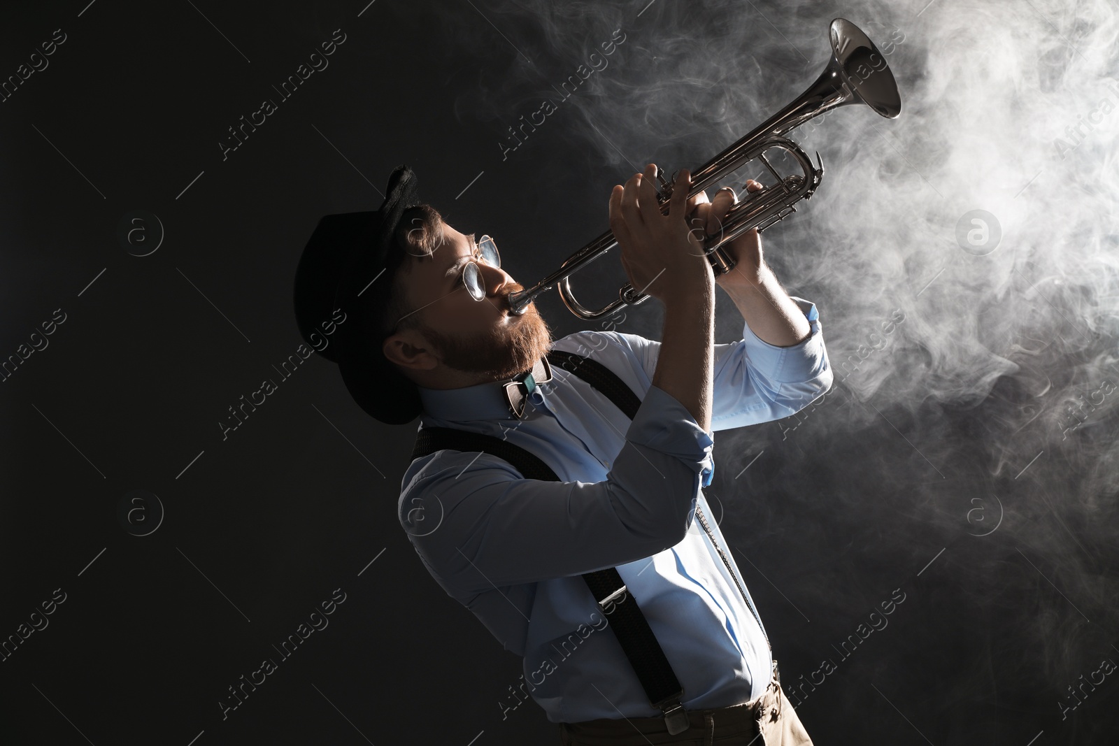 Photo of Professional musician playing trumpet on black background with smoke