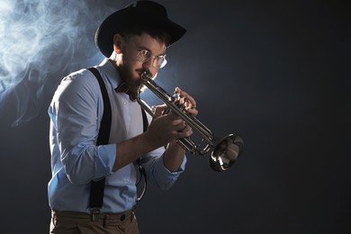 Photo of Professional musician playing trumpet on dark background with smoke. Space for text