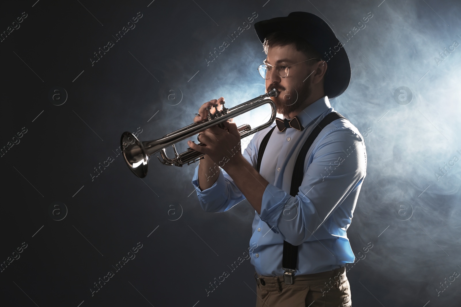 Photo of Professional musician playing trumpet on dark background with smoke