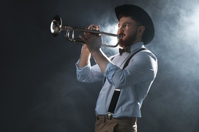 Photo of Professional musician playing trumpet on dark background with smoke