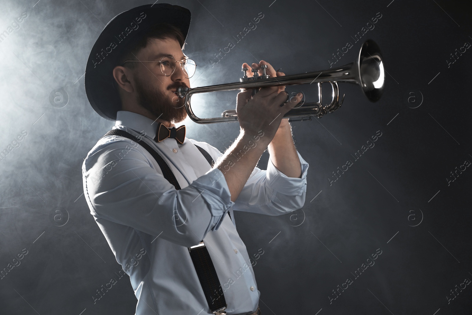 Photo of Professional musician playing trumpet on dark background with smoke