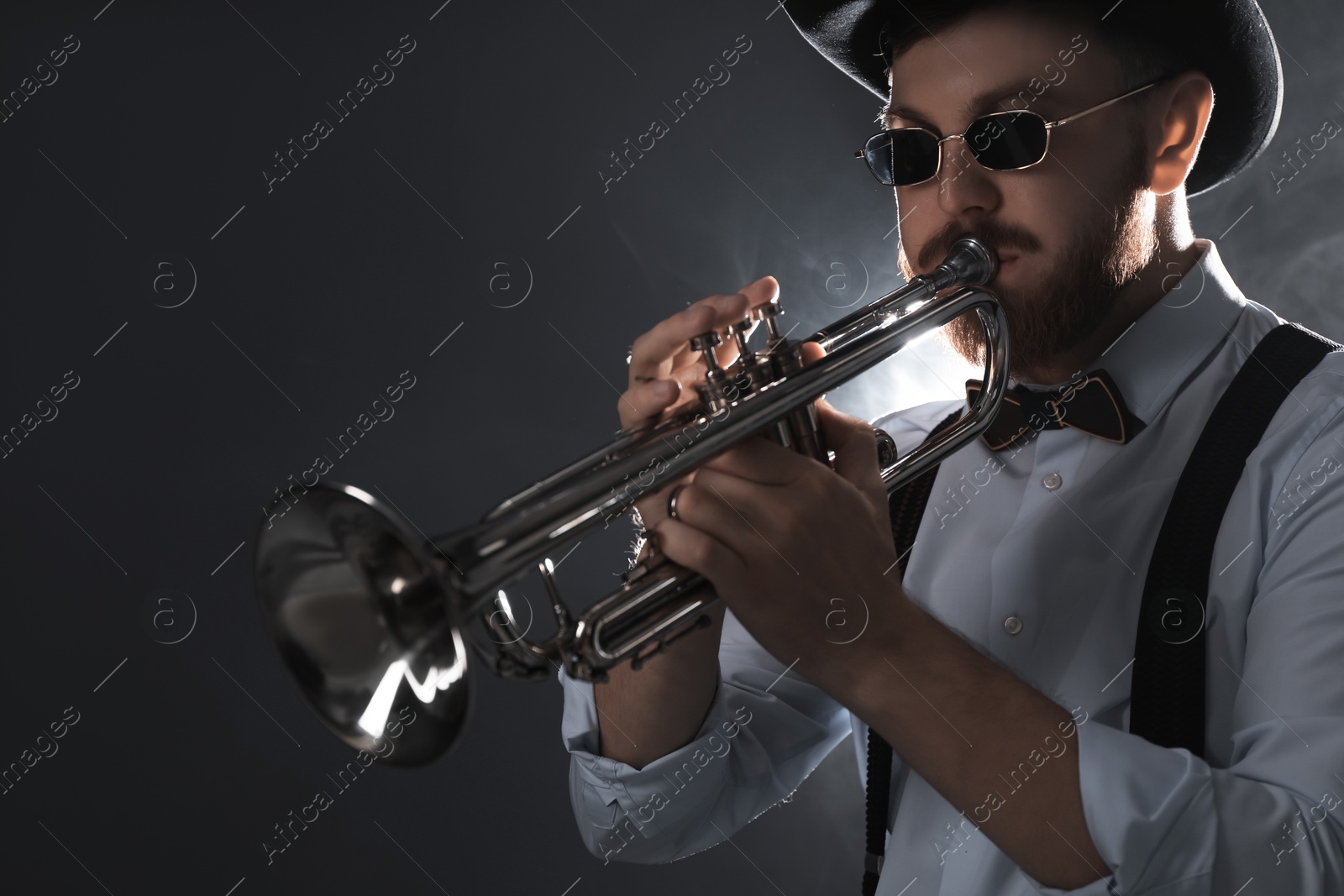 Photo of Professional musician playing trumpet on dark background with smoke