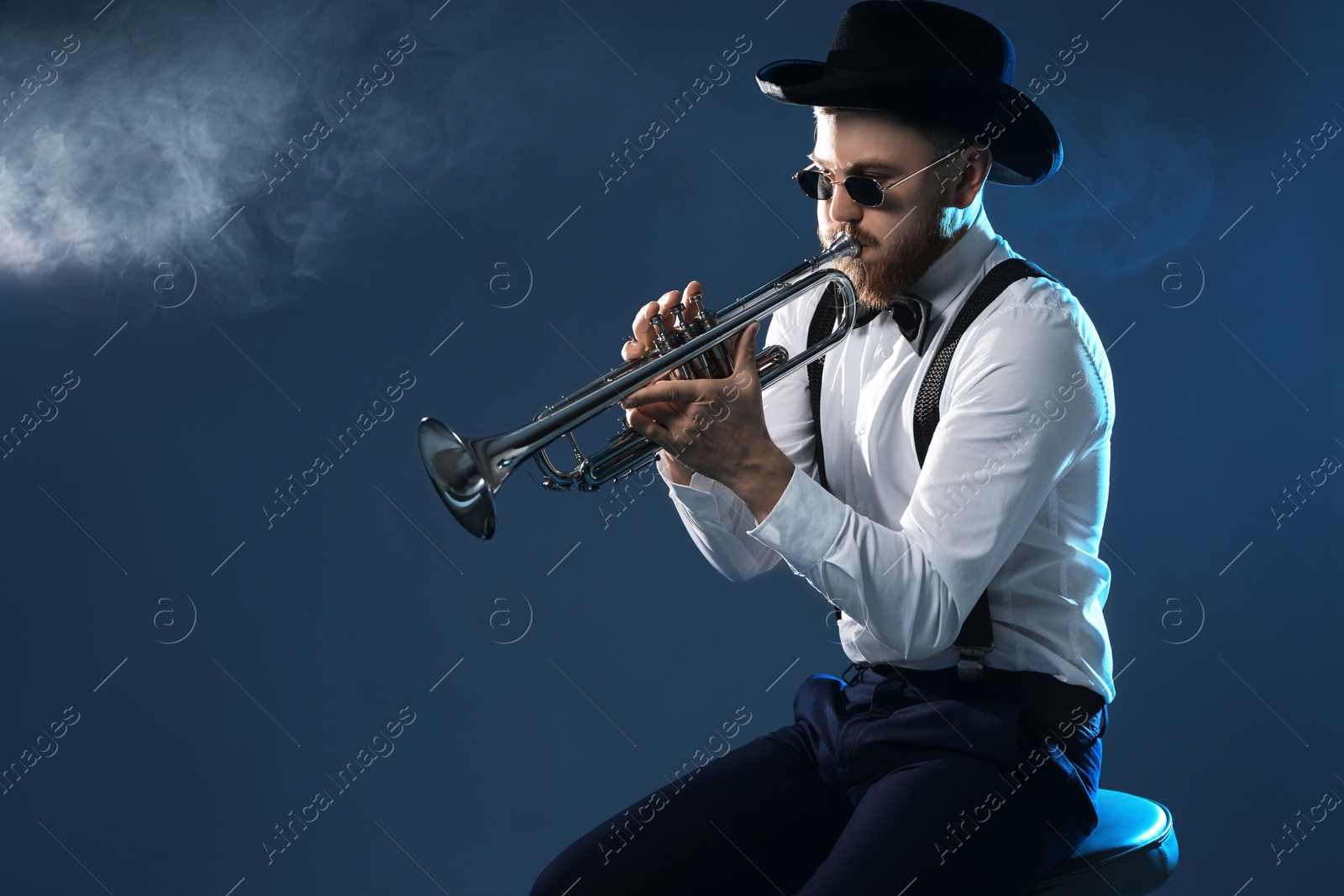 Photo of Professional musician playing trumpet on dark background with smoke. Space for text