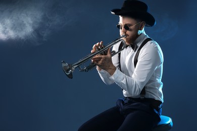 Professional musician playing trumpet on dark background with smoke. Space for text