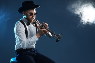 Photo of Professional musician playing trumpet on dark background with smoke. Space for text