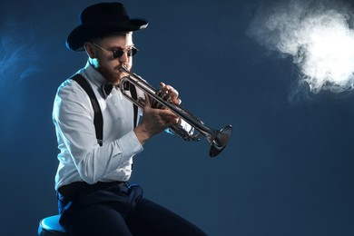 Professional musician playing trumpet on dark background with smoke. Space for text