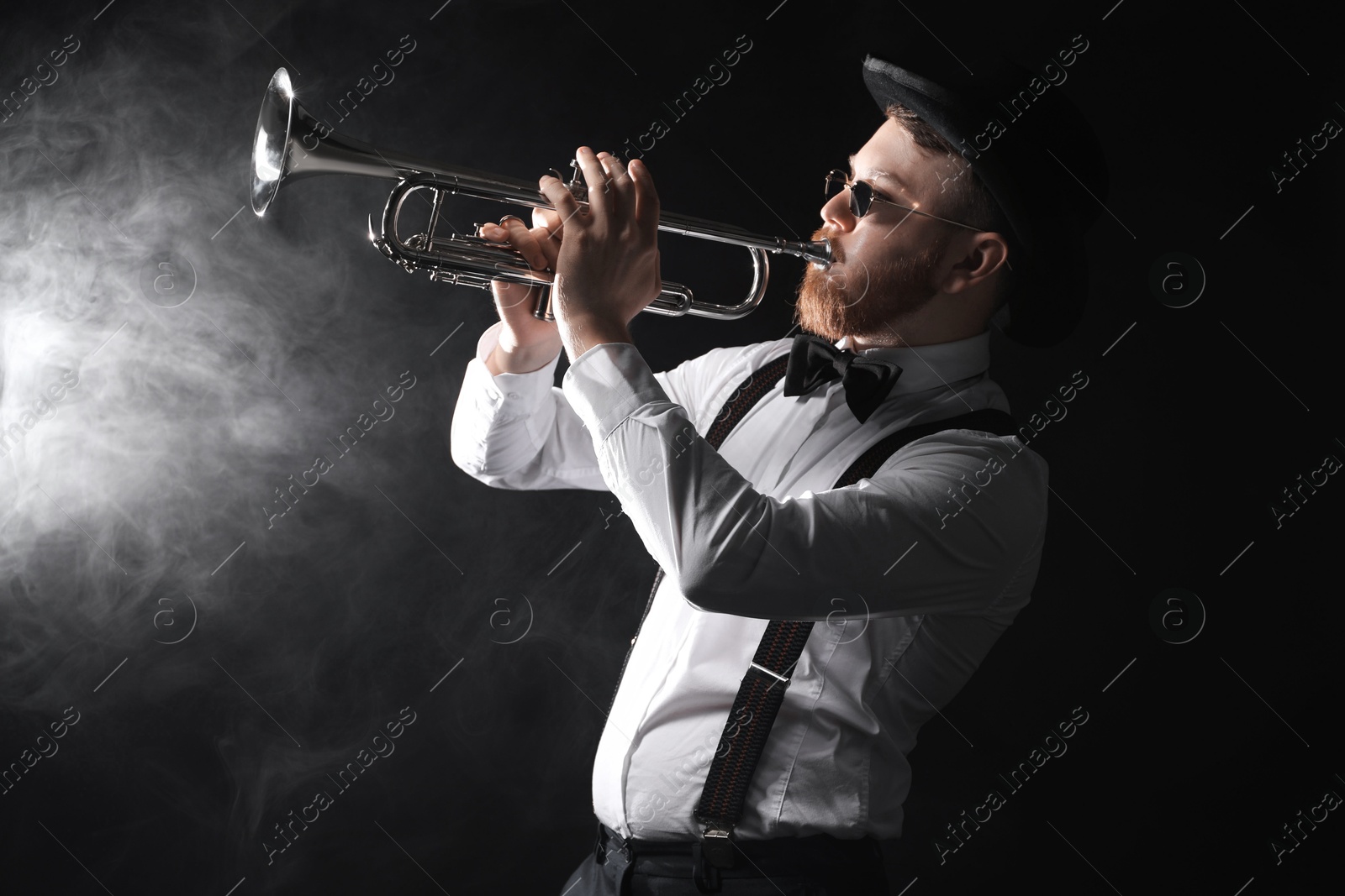 Photo of Professional musician playing trumpet on black background with smoke