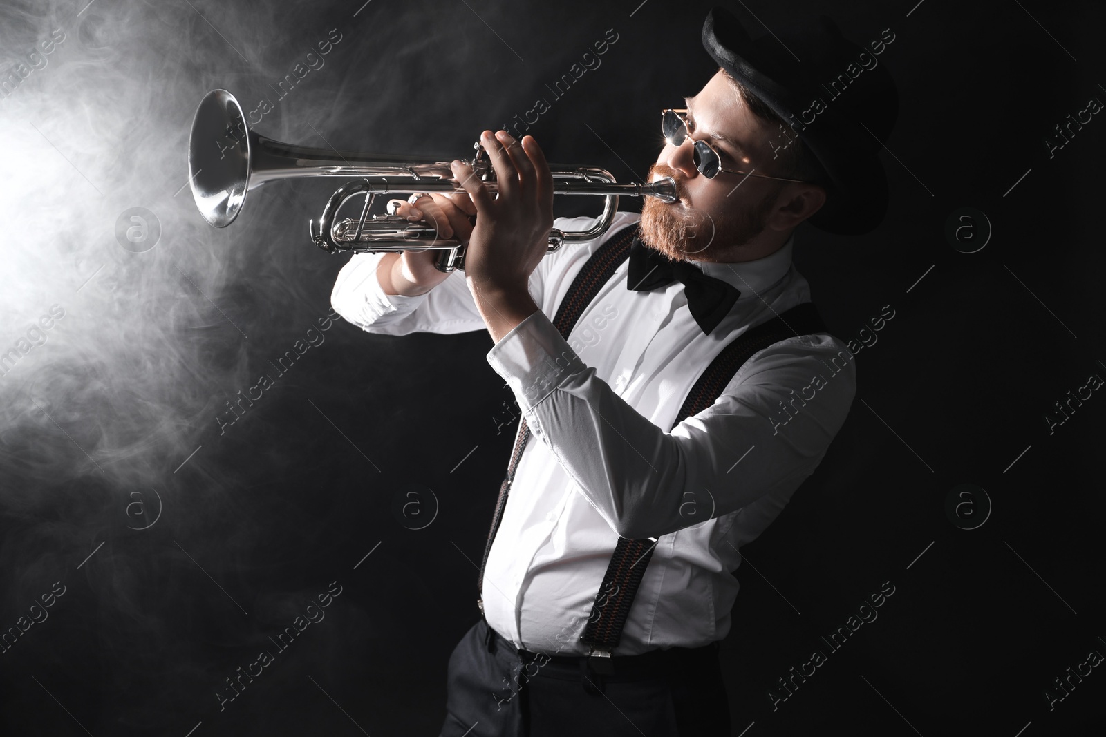 Photo of Professional musician playing trumpet on black background with smoke