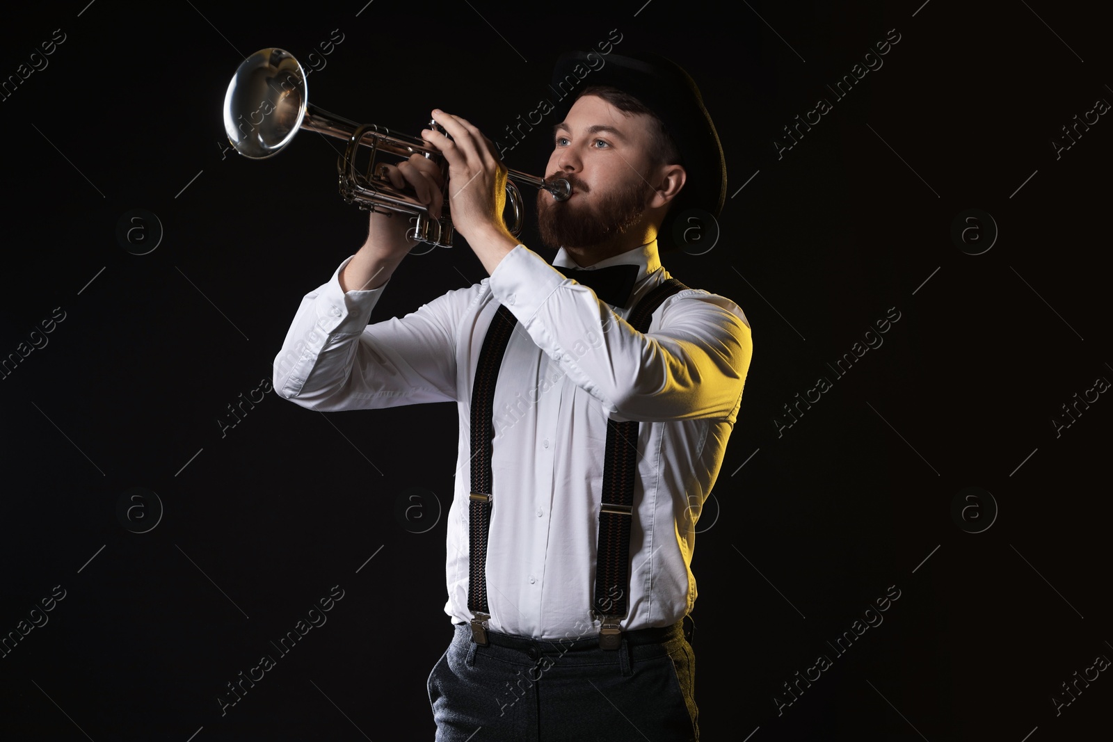 Photo of Professional musician playing trumpet on black background in color lights