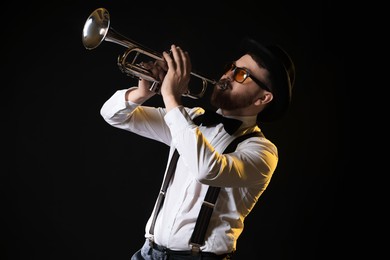 Photo of Professional musician playing trumpet on black background in color lights