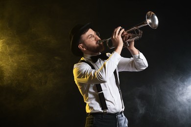 Photo of Professional musician playing trumpet on black background in color lights and smoke