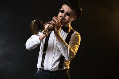 Photo of Professional musician playing trumpet on black background in color lights